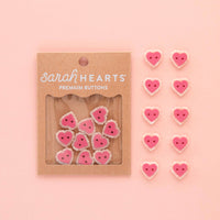 Heart-shaped buttons with 'sarahHEARTS' packaging on a pink background