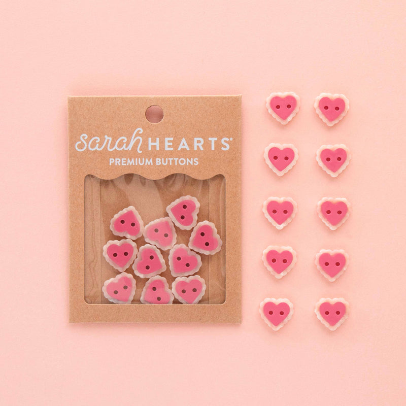 Heart-shaped buttons with 'sarahHEARTS' packaging on a pink background