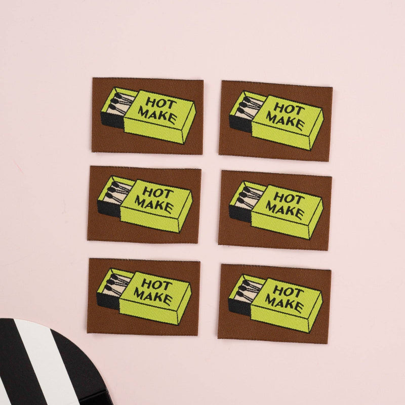Five woven labels with matchbox with 'Hot Make' text on a pink background