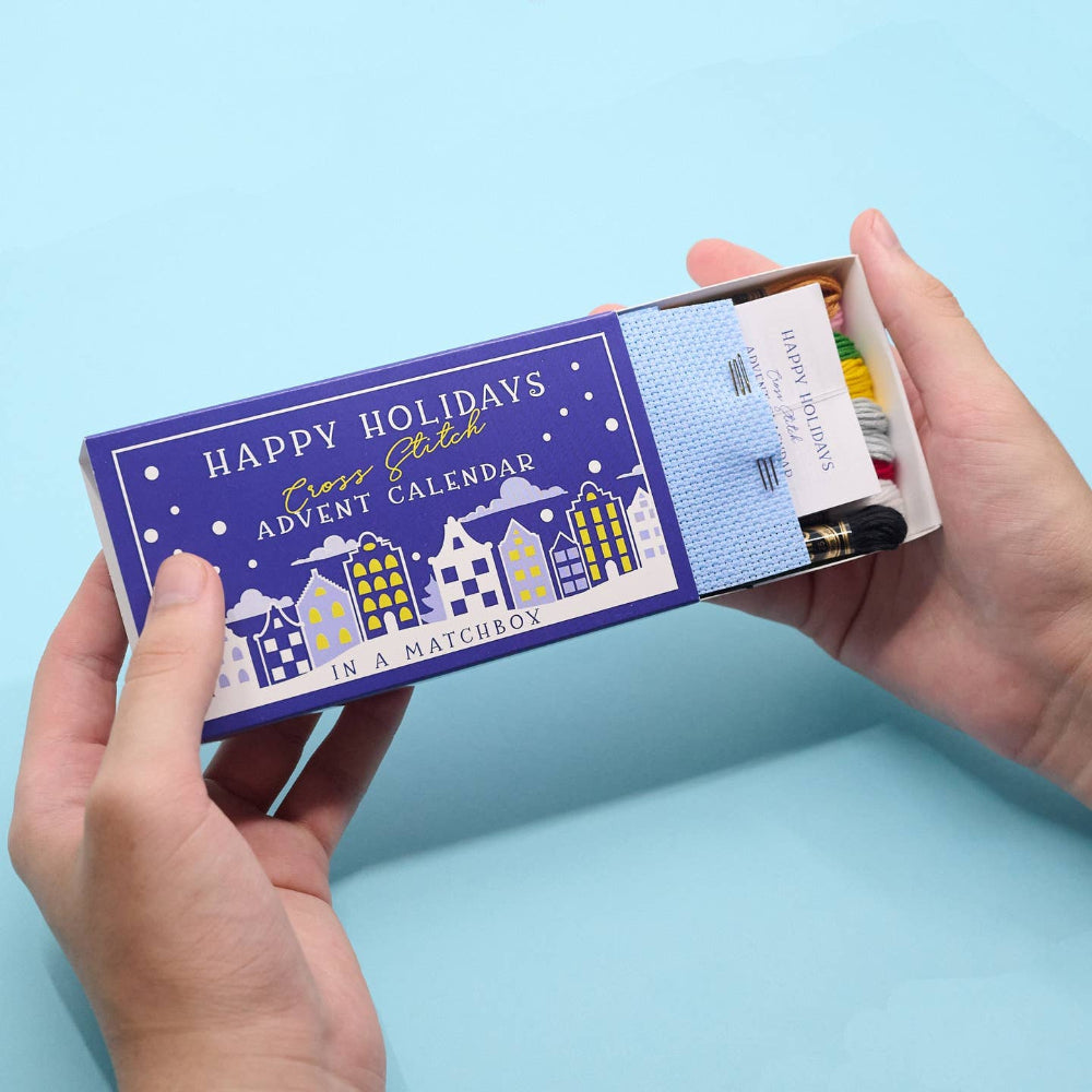 Hand holding a matchbox advent calendar with a blue label on a light blue background