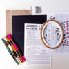Embroidery kit with cross-stitch pattern, hoop, fabric, and colorful threads on a white background.