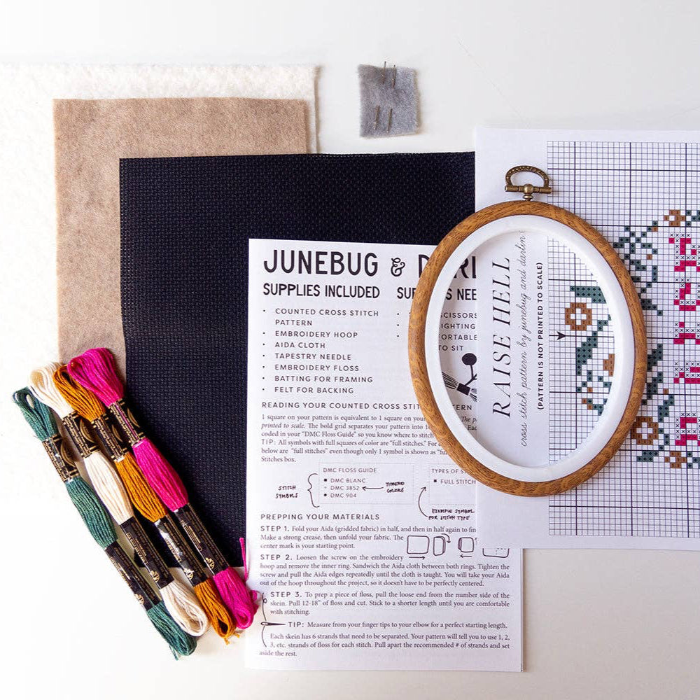 Embroidery kit with cross-stitch pattern, hoop, fabric, and colorful threads on a white background.