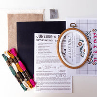 Embroidery kit with cross-stitch pattern, hoop, fabric, and colorful threads on a white background.