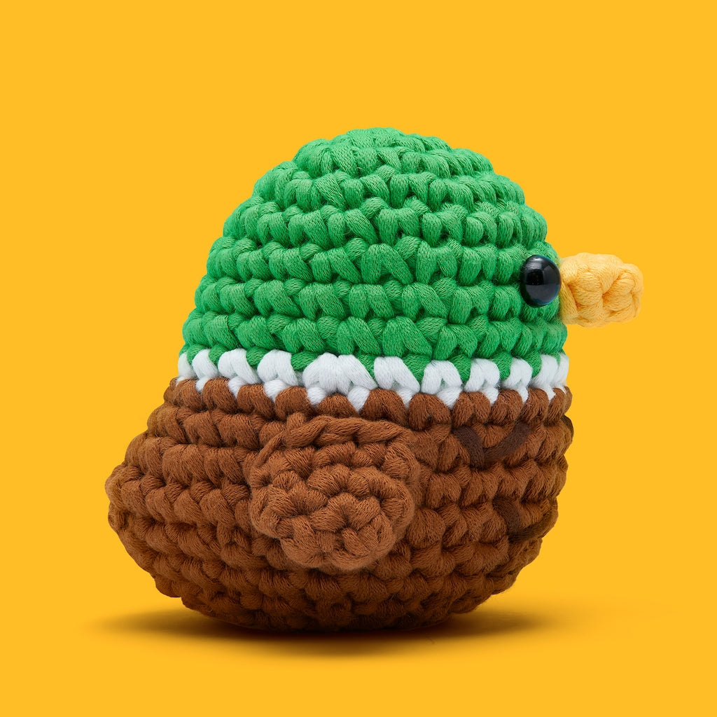 Crocheted mallard toy with green head, brown body, and yellow beak on a yellow background