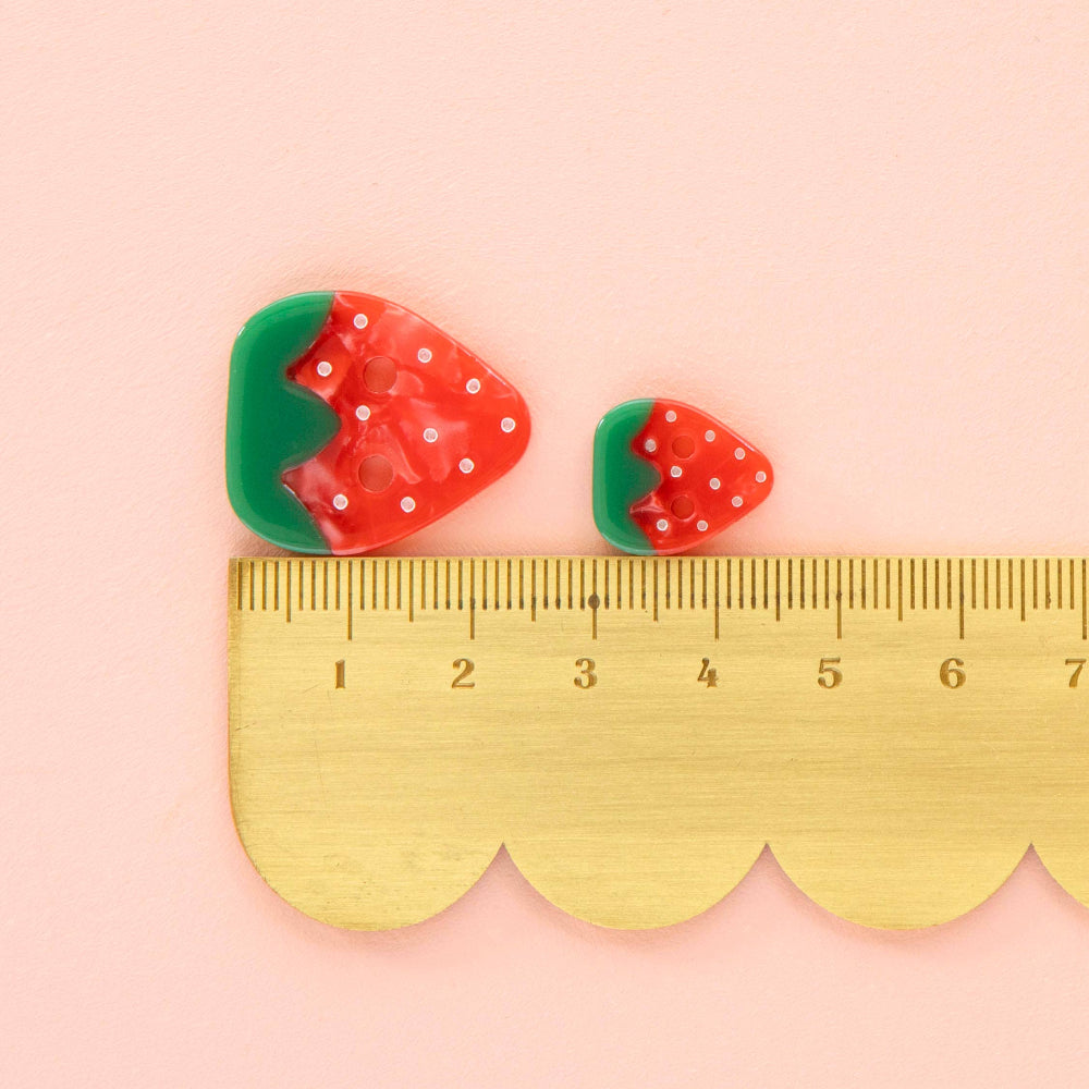 Strawberry-shaped buttons with a ruler on a pink background