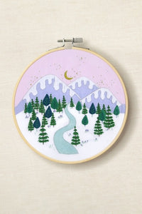 Embroidery hoop with a winter landscape design featuring trees, mountains, and a river.