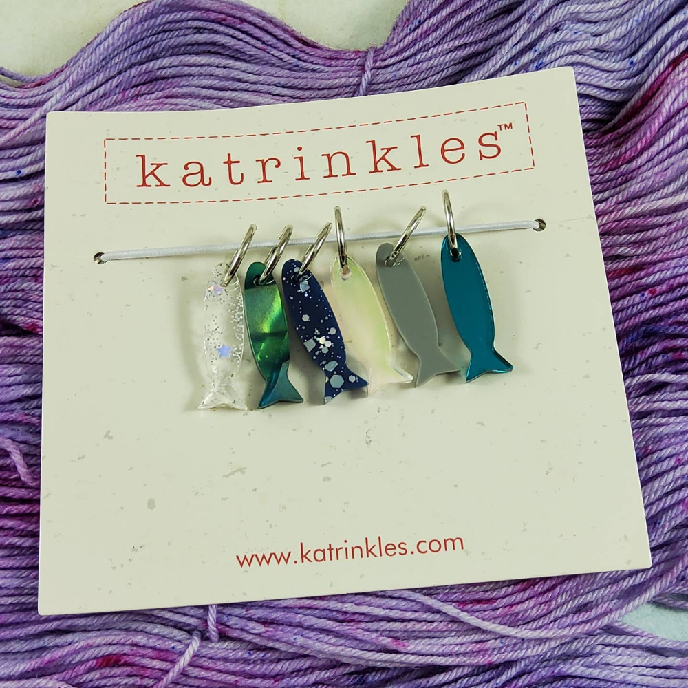 Katrinkles packaging containing 6 fish shaped stitch markers on top of purple yarn