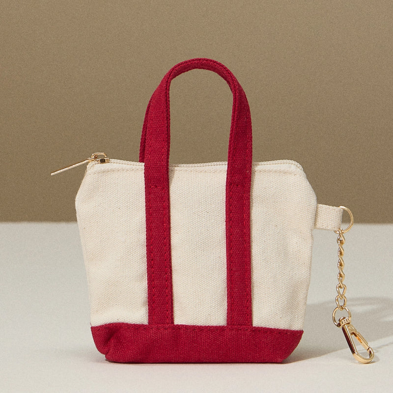Mini tote bag with red bottom and handles, zip top, and key chain on the side.