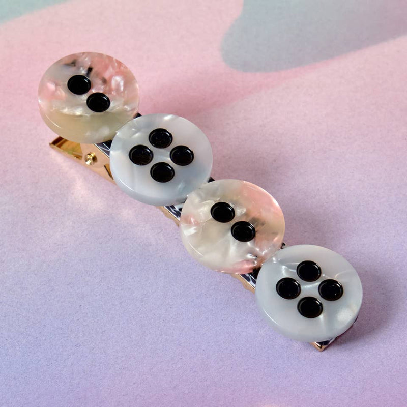 Hair clip with four round buttons on a pink background