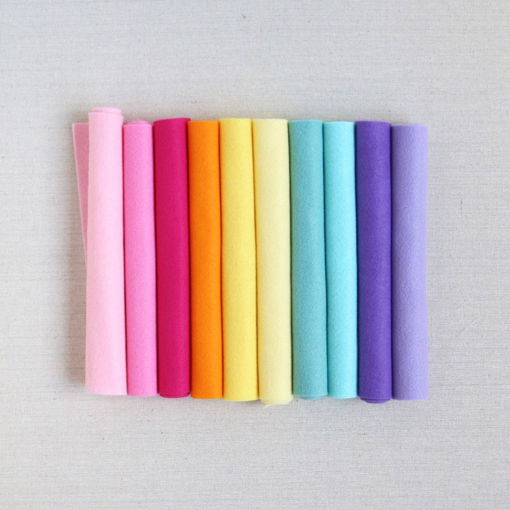 Various shades of felt sheet rolls in pinks, oranges, yellows, blues, and purples on a textured white background