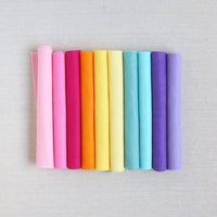 Various shades of felt sheet rolls in pinks, oranges, yellows, blues, and purples on a textured white background