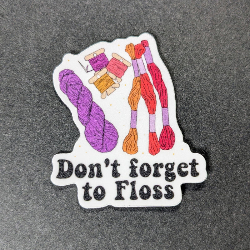 Sticker with yarn and text 'Don't forget to Floss' on a dark background