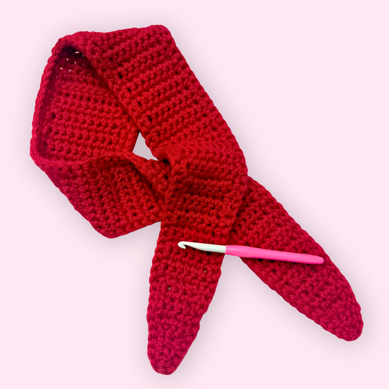 Red crocheted scarf with a pink crochet hook on a white background