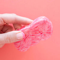 Hand holding a pink yarn skein shaped hair claw against a pink background