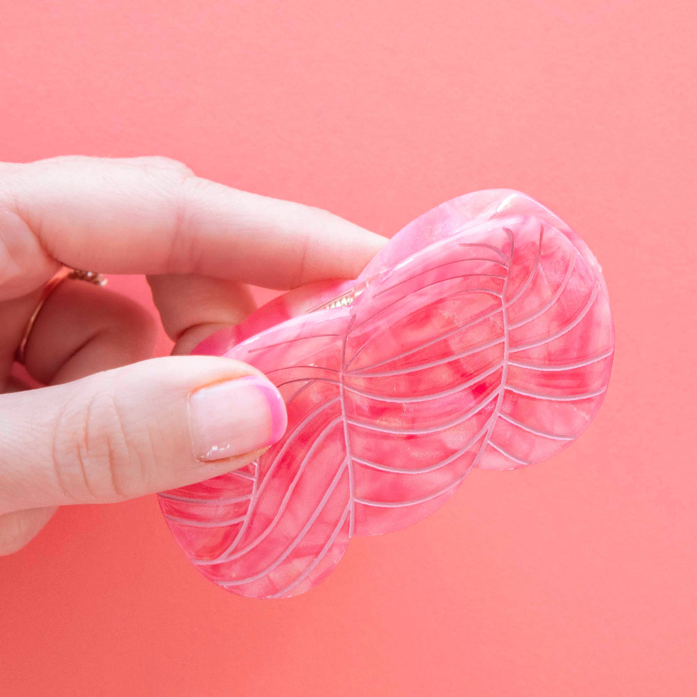 Hand holding a pink yarn skein shaped hair claw against a pink background