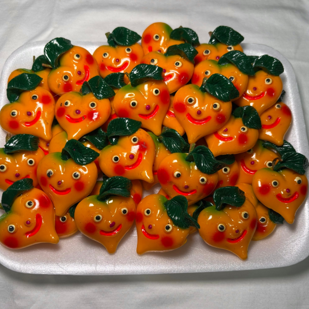 white tray of peach shaped magnets. Each peach has a smiley face, rosy cheeks, and a green leaf on top.
