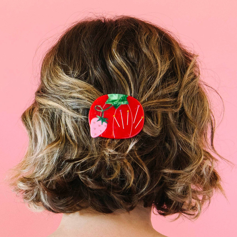 Person with a red hair clip featuring a tomato design on a pink background