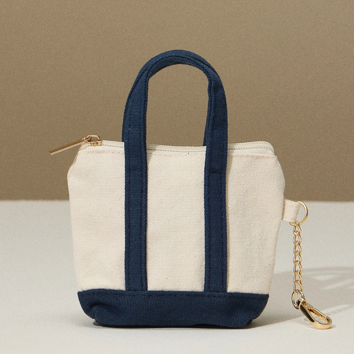 Mini tote bag with navy bottom and handles, zip top, and key chain on the side.