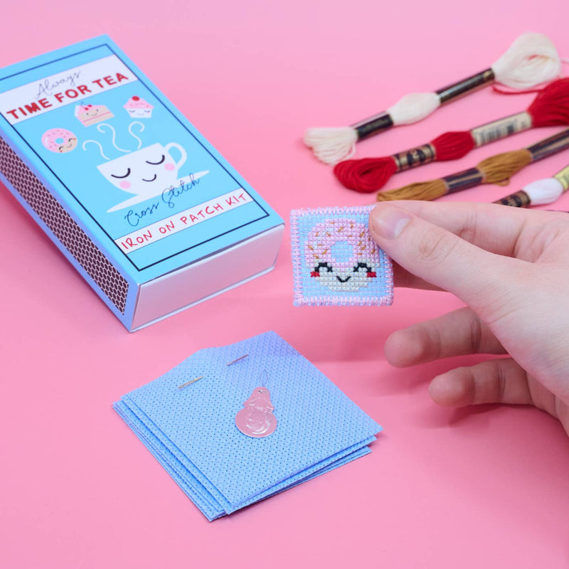 Cross-stitch kit with a hand holding a completed patch on a pink background