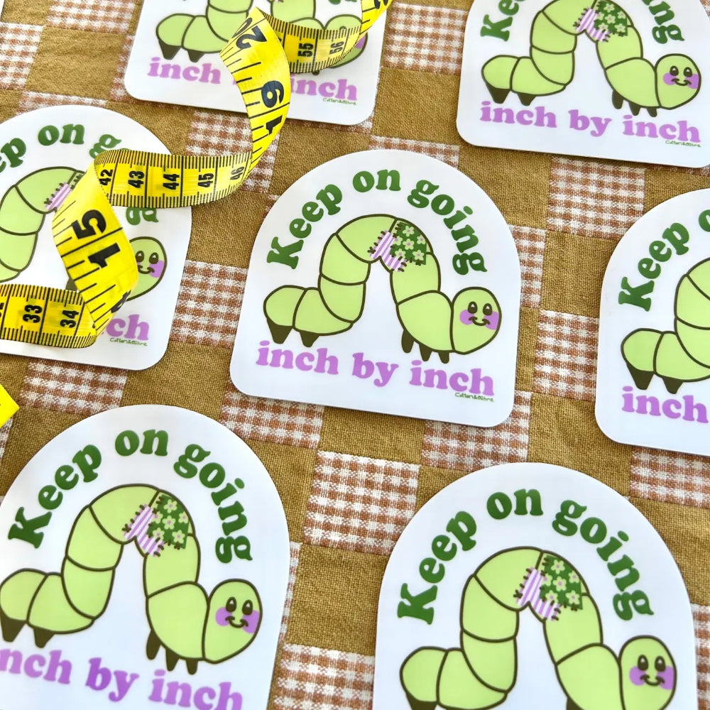 Stickers with green caterpillar illustrations and motivational text on a checkered fabric background