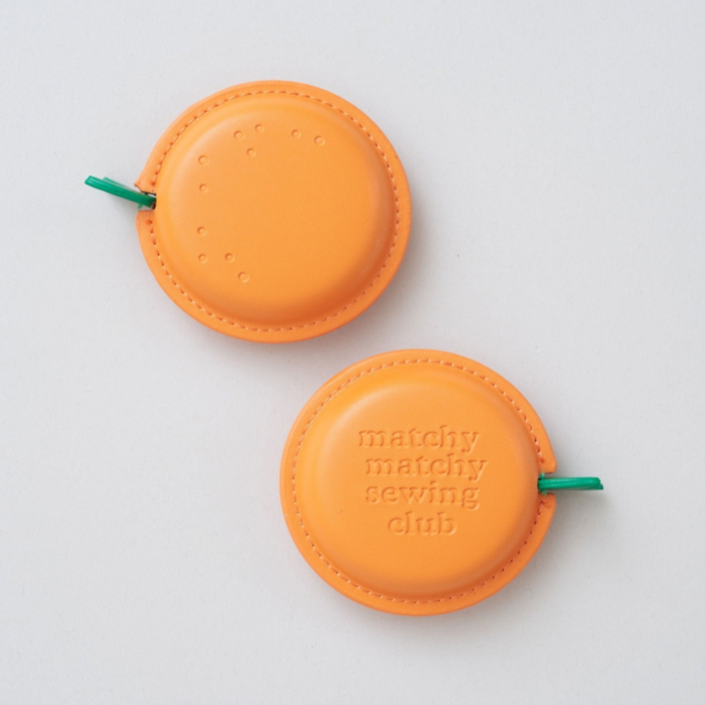 Two orange measuring tapes with 'matchy matchy sewing club' branding on a light gray background.
