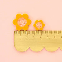 Yellow flower-shaped buttons with a ruler on a pink background