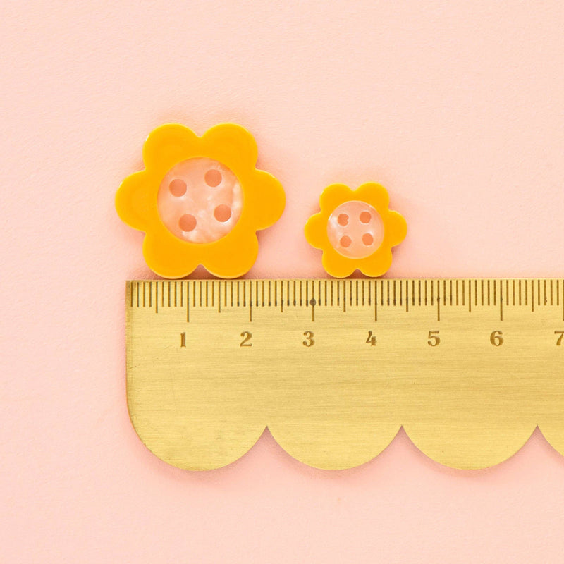 Yellow flower-shaped buttons with a ruler on a pink background