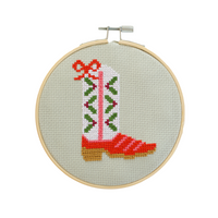 Cross-stitched cowboy boot in an embroidery hoop on a light green background