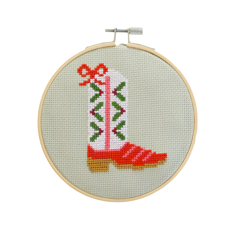 Cross-stitched cowboy boot in an embroidery hoop on a light green background