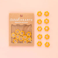 Packaged yellow flower buttons with 'Sarah Hearts' branding on a pink background