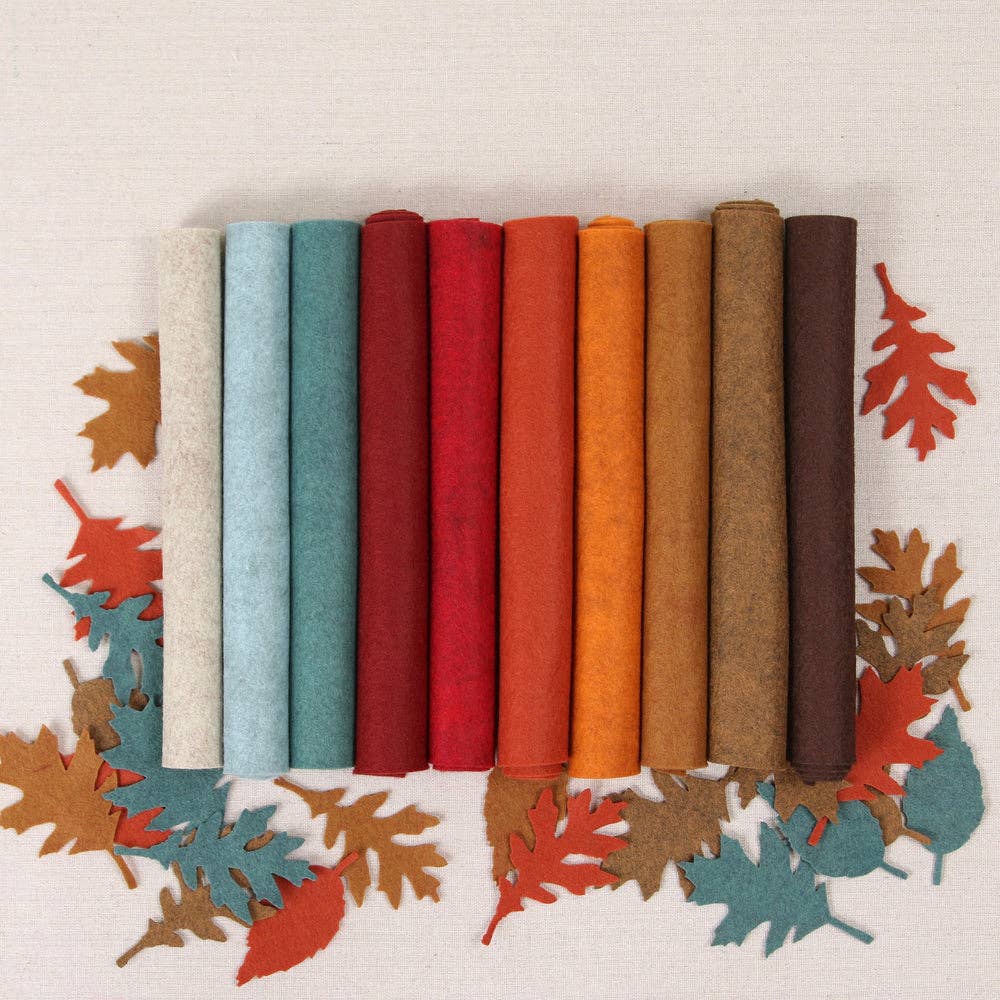 Ten rolls of autumnal felt shades in blues, reds, oranges, and browns on top of multicolor paper leaf cutouts on a white textured background