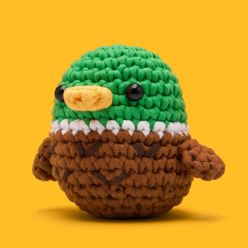 Crocheted bird toy with green head, brown body, and yellow beak on a yellow background