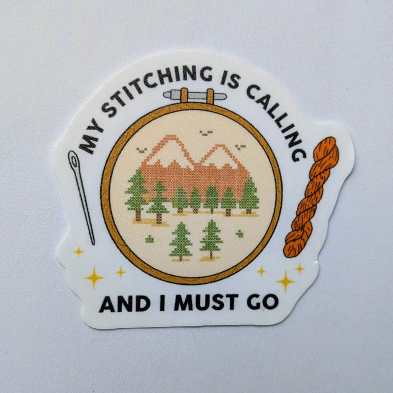 Sticker with cross-stitch design and text 'My stitching is calling and I must go' on a light gray background