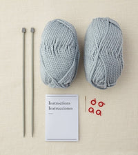 Two skeins of light blue yarn, knitting needles, and a card with text on a beige background