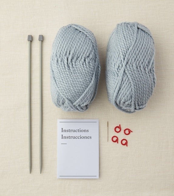 Two skeins of light blue yarn, knitting needles, and a card with text on a beige background