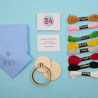 cross stitch kit with threads, hoop, and cards on a blue background