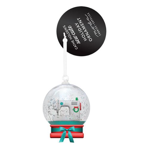 Snowglobe ornament with a white sewing machine inside and a pink base with a blue bow.