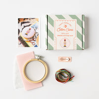 Cross-stitch kit with hoop, thread, and box on a white background