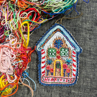 Embroidered gingerbread house patch with colorful threads on a textured fabric background