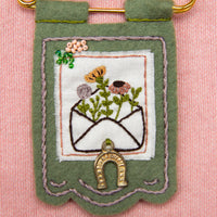 Embroidered banner with floral design and gold elements on a pink background