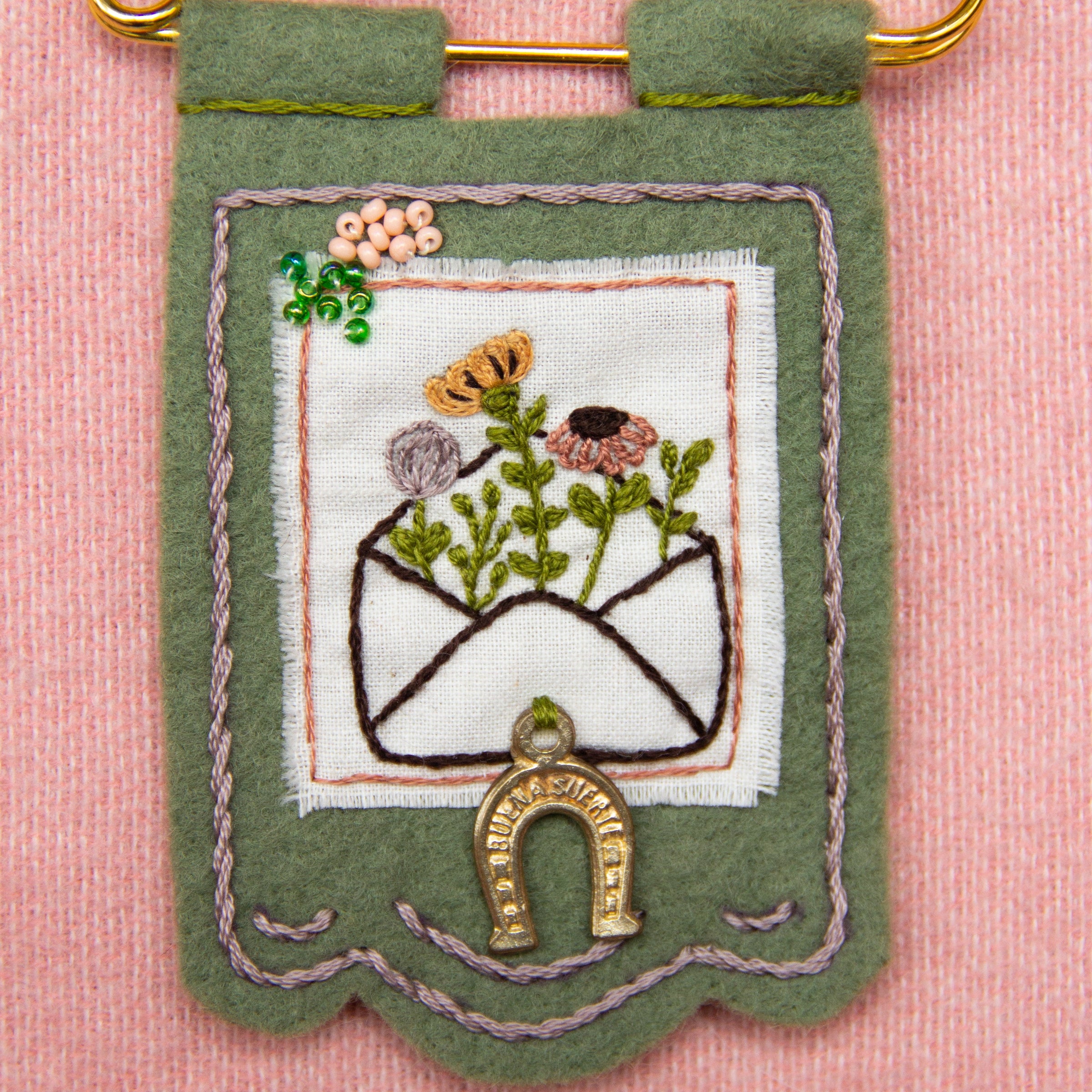 Embroidered banner with floral design and gold elements on a pink background