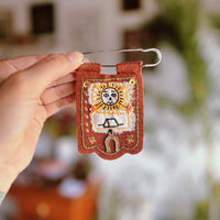 Hand holding a small embroidered keychain with a sun design against a blurred background