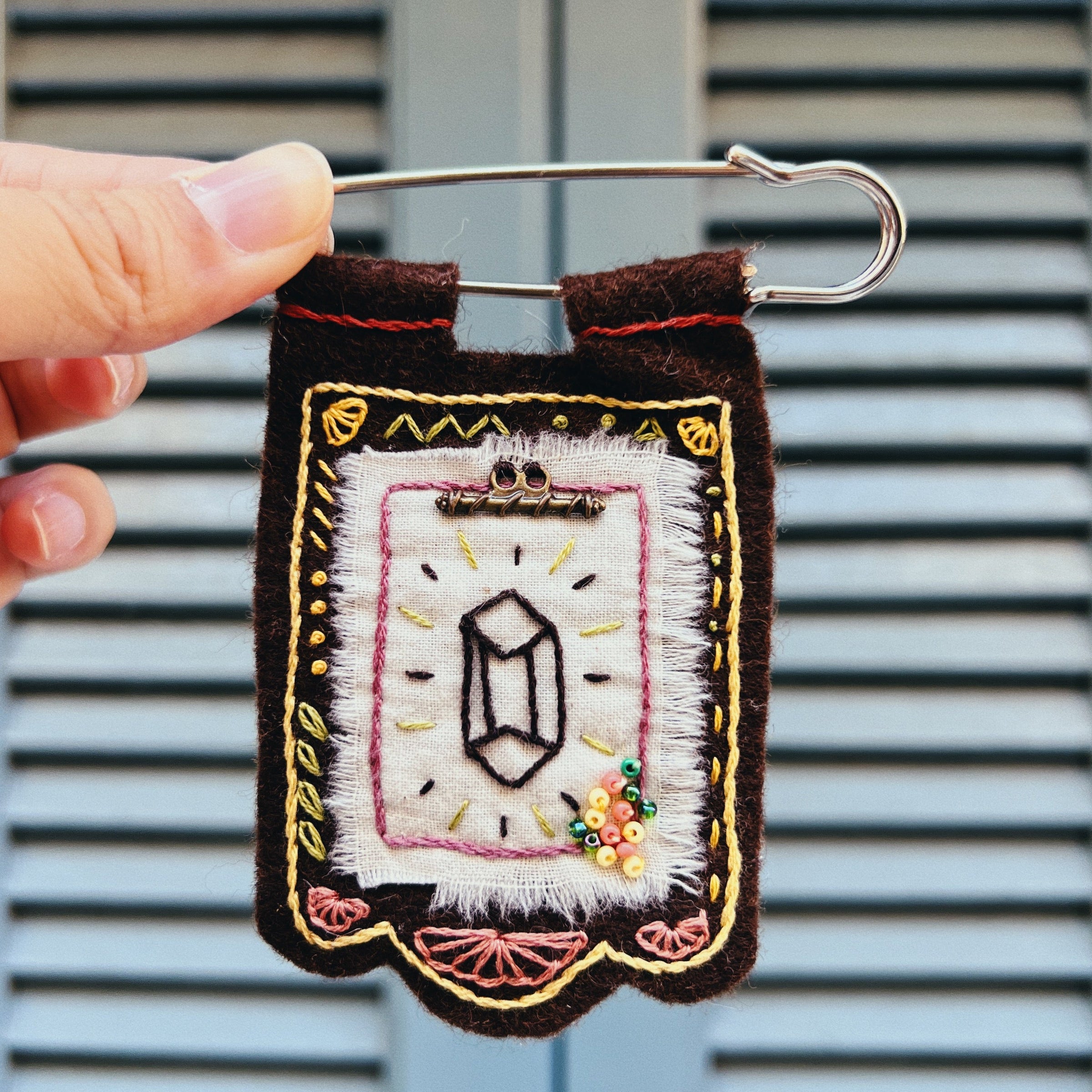 Embroidered patch on a safety pin held against a window blind background