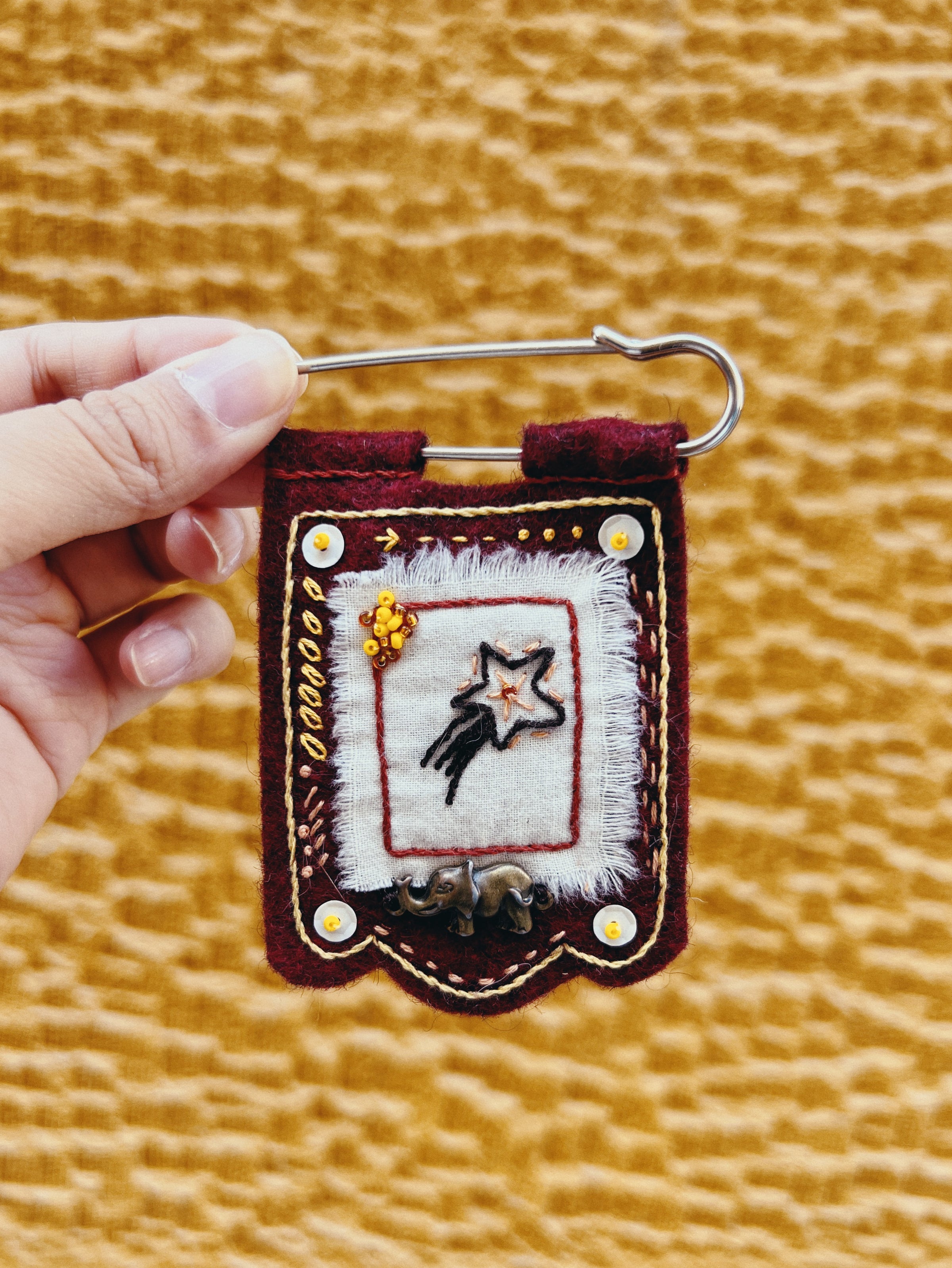 Handmade embroidered keychain with a star design held by a hand against a textured yellow background