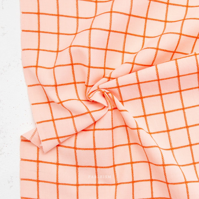 A close-up of peach-colored fabric with an orange grid pattern, gathered in the center against a light textured background.