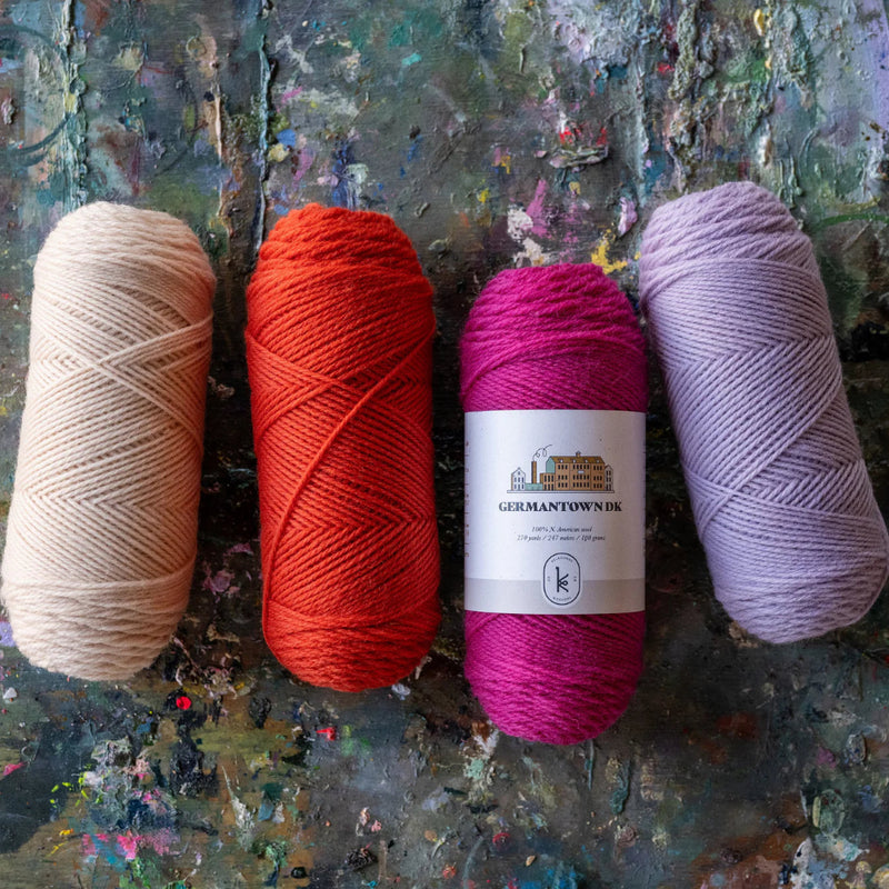 Skeins of dk yarn in beige, orange, fuschia and lilac on a painted surface. 
