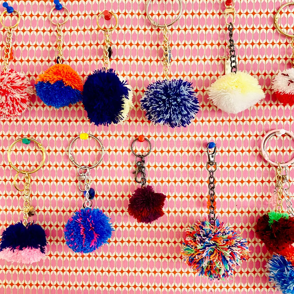 Colorful pom-pom keychains on a pink patterned background