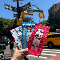 A hand holds three small custom photo frames decorated with rhinestones and blue beads, set against a busy New York City street background with a yellow cab and pedestrians.