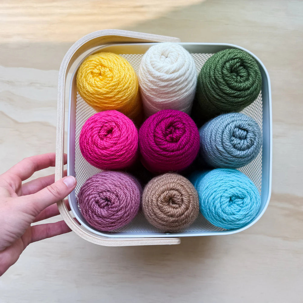 Hand holding a container with colorful yarn balls on a wooden surface