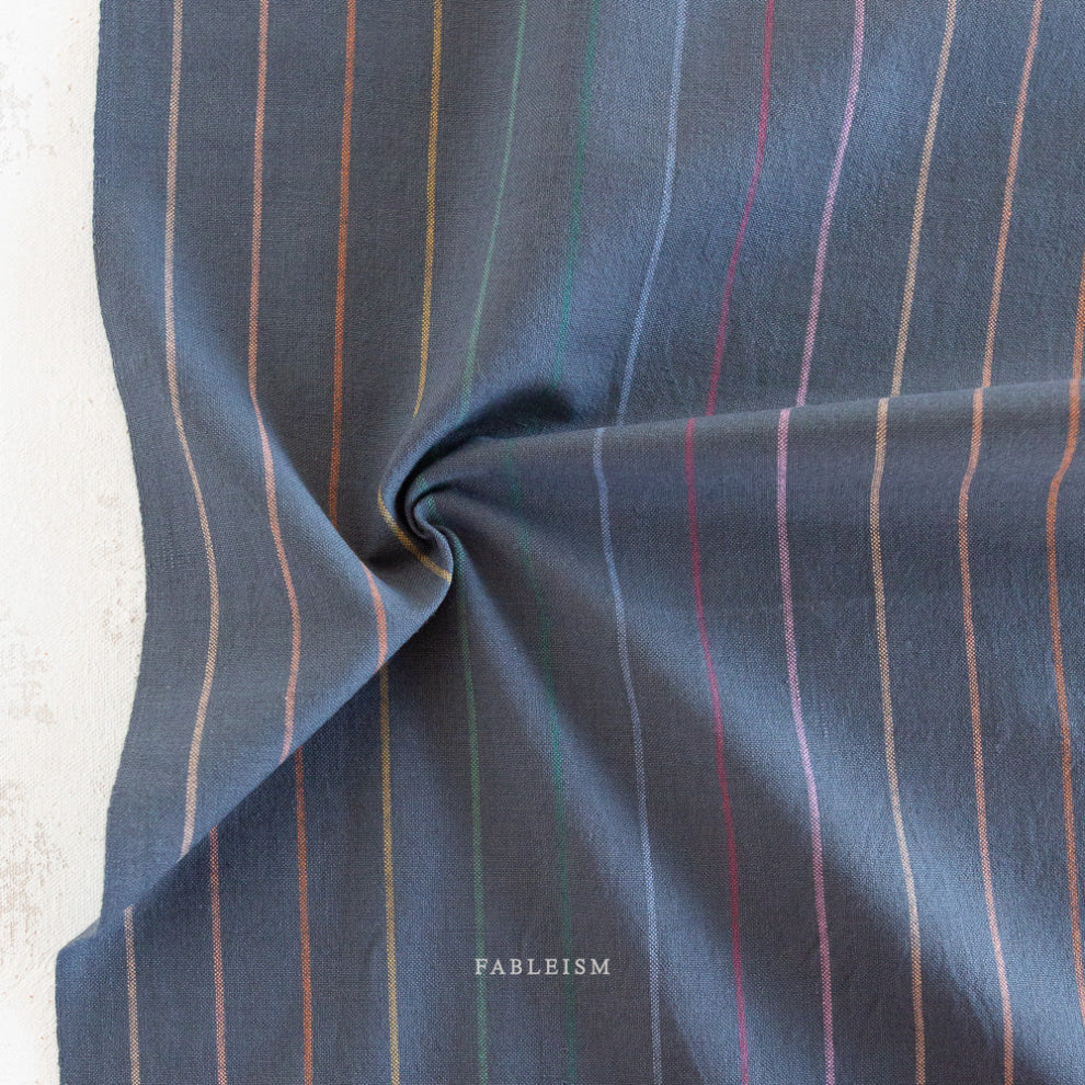 Striped dark fabric with vertical lines in various colors on a neutral background, featuring the brand 'Fableism'.